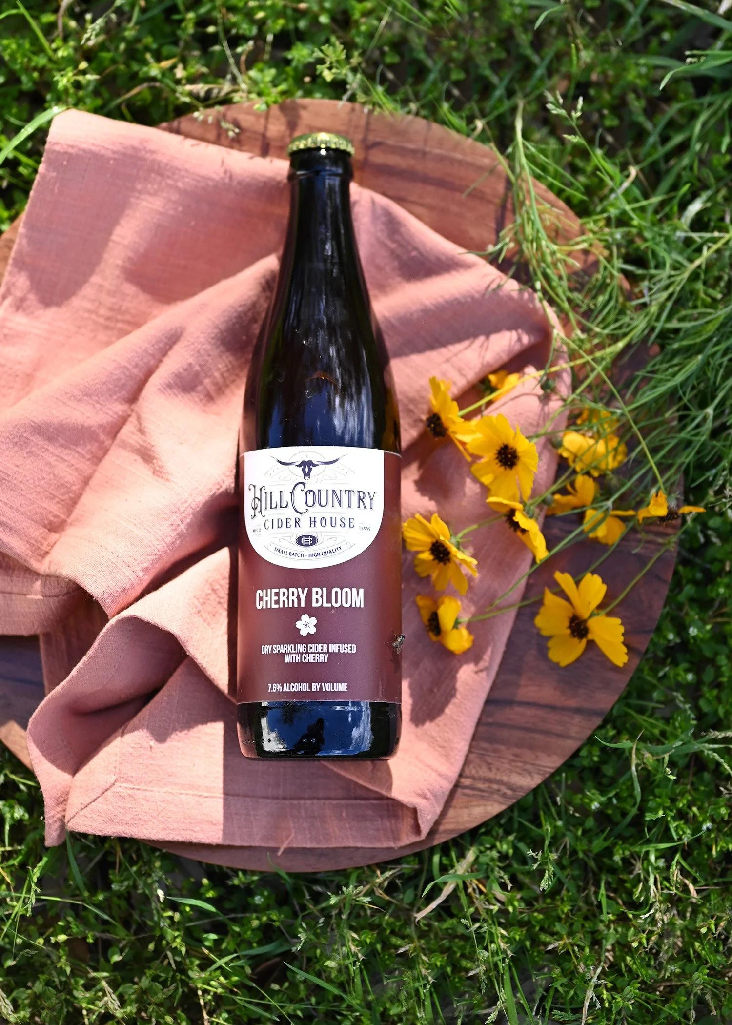 Cherry Bloom cider on pink cloth with yellow flowers