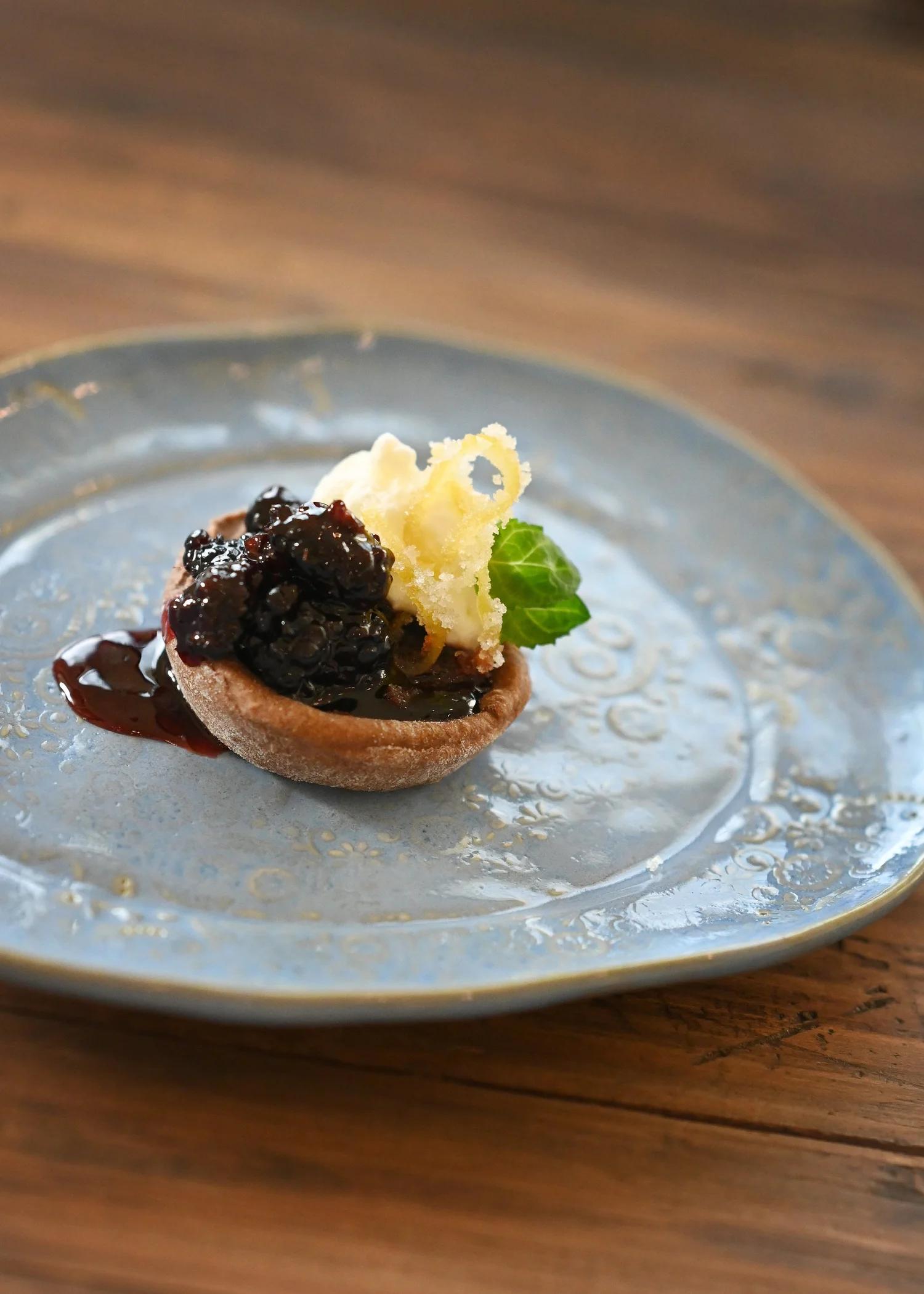 Plated dessert with blueberry jam, whipped cream, mint and candied lemon