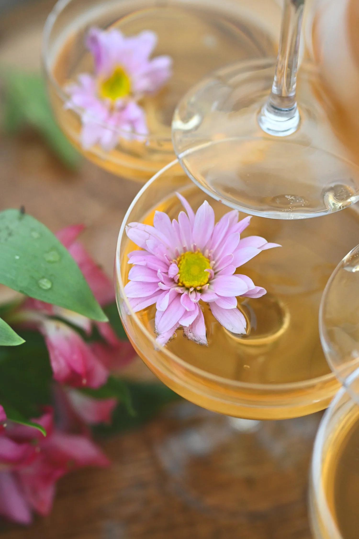 Three flutes of cider with pink flowers on a wooden surface