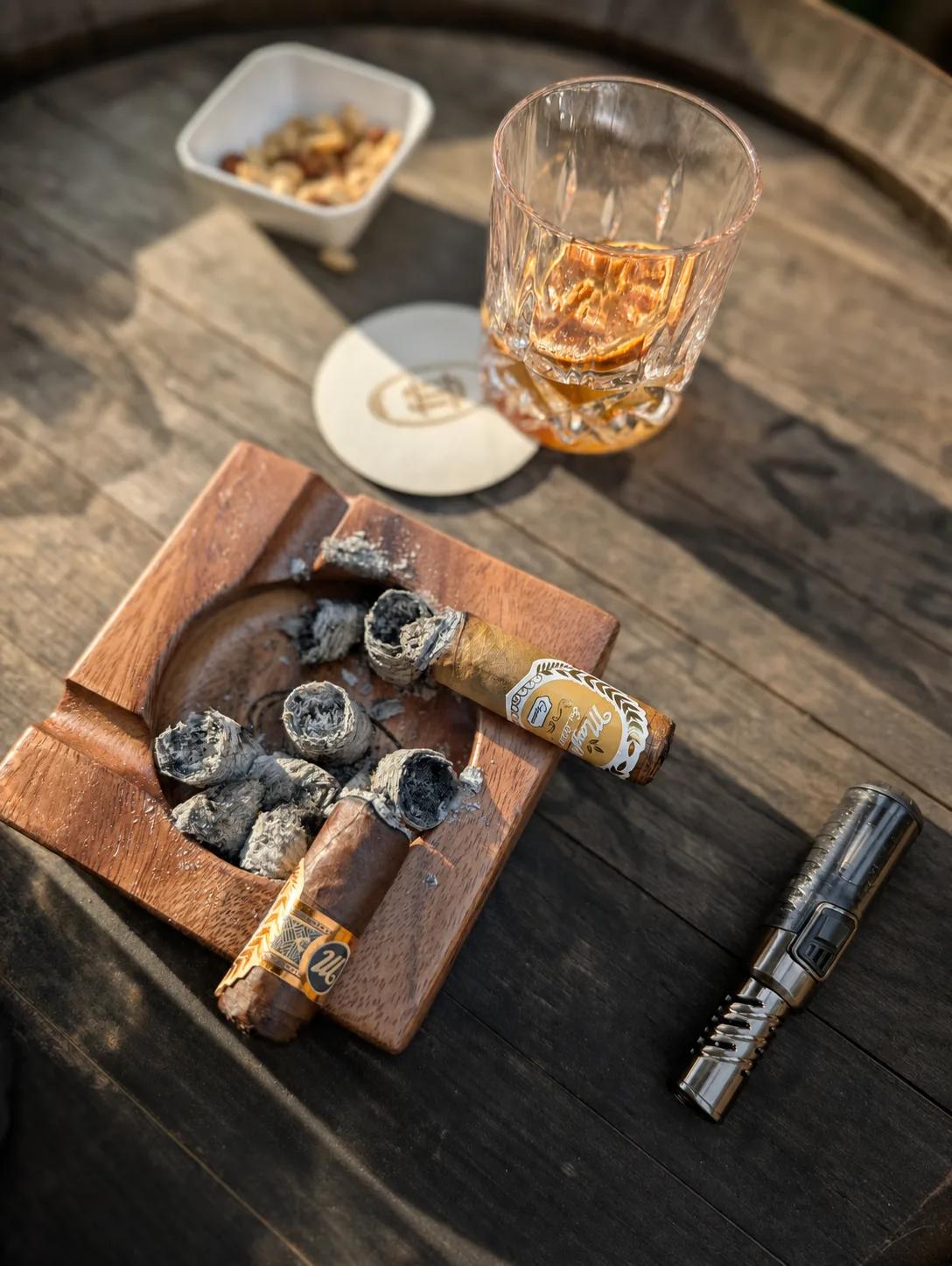 Two Mayfin cigars in an ashtray beside a glass of cider on a barrel top