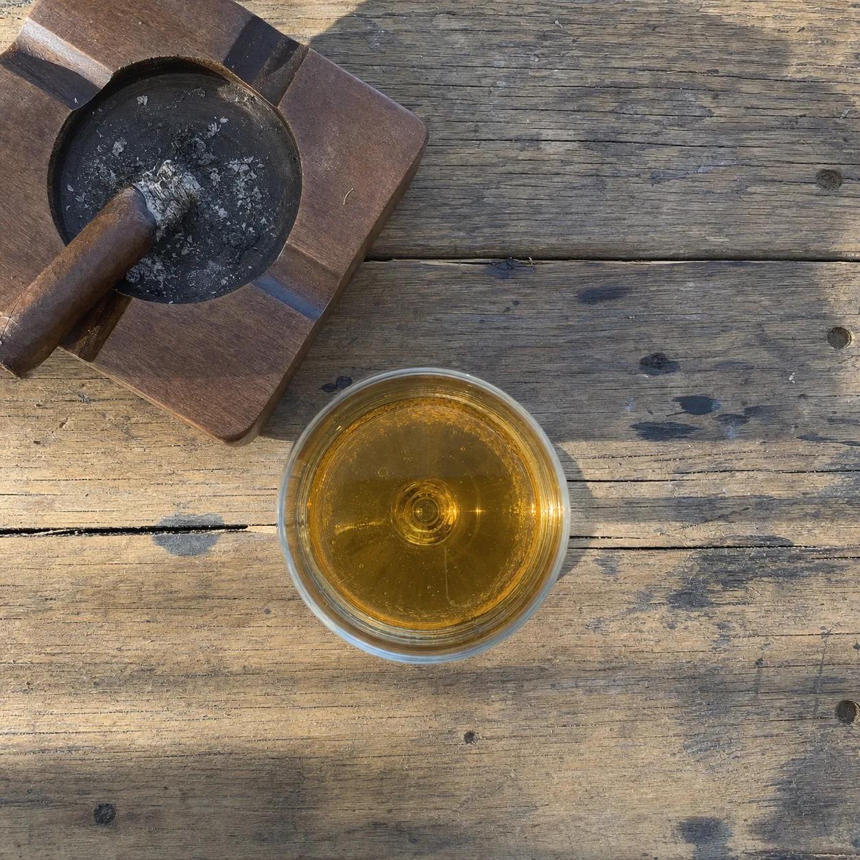 A cigar resting in an ashtray beside a glass of cider, seen from above