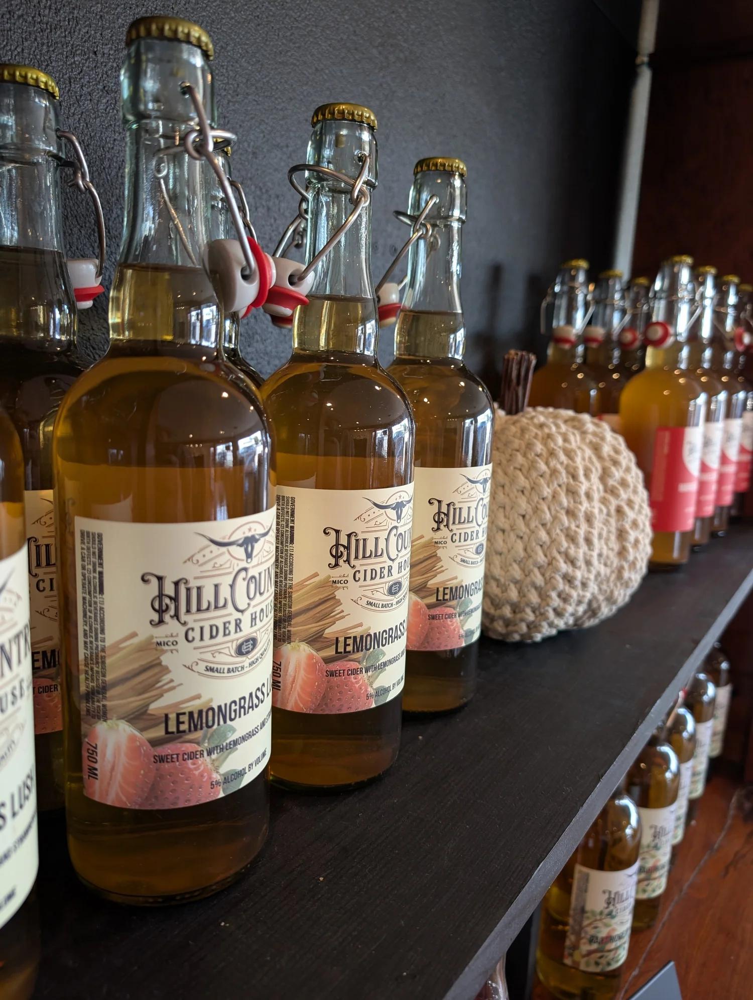Lemongrass and strawberry cider bottles with swing-top caps on a dark wooden shelf